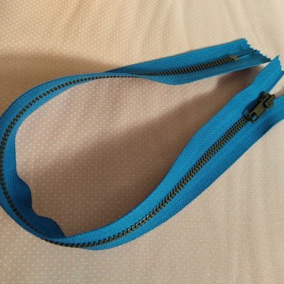 Fecho éclair azul com dentes e cursor pretos sobre tecido bege com pontos brancos.