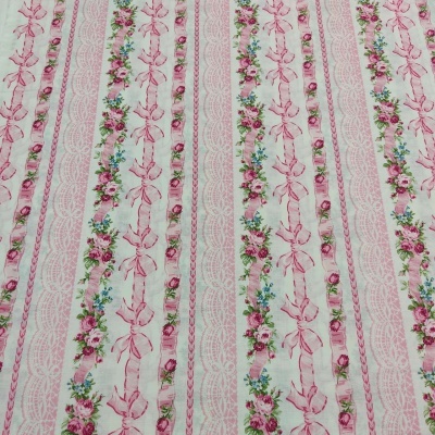 Tecido branco com faixas verticais de flores, laços e rendas cor-de-rosa