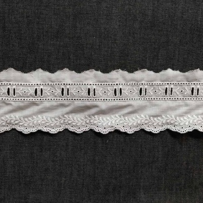 Fita de tecido branca decorativa com padrões de buracos e bordados sobre fundo preto.