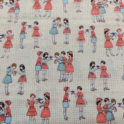 Tecido estampado com meninas em vestidos e saias vermelhas, azuis e brancas sobre fundo quadriculado bege