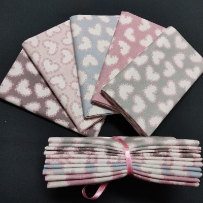 Conjunto de tecidos com padrão de corações em rosa, azul e cinza sobre fundo preto.