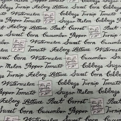 Tecido branco com palavras de legumes e frutas em escrita cursiva preta e três etiquetas manuscritas pequenas