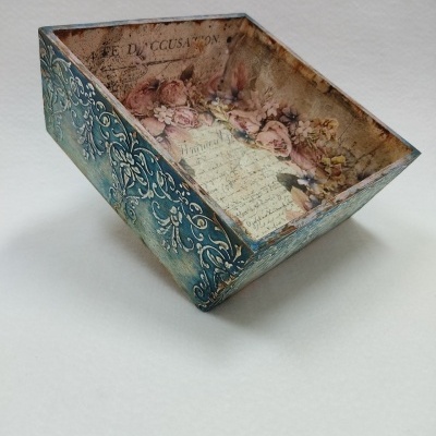 Caixa decorativa trapezoidal com padrão floral azul e texto em francês no interior