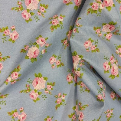 Tecido azul claro com padrão de rosas cor-de-rosa e folhas verdes