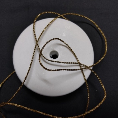 Objeto redondo branco com furo central e fio metálico dourado