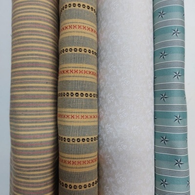 Quatro rolos de tecido com padrões variados e cores neutras e azul esverdeado