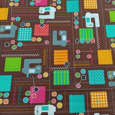 Tecido colorido com padrão de máquinas de costura, quadrados coloridos e botões sobre fundo castanho