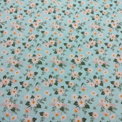 Tecido azul claro com padrão floral branco e amarelo com folhas verdes