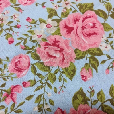 Tecido com padrão floral de rosas cor-de-rosa e folhas verdes em fundo azul claro