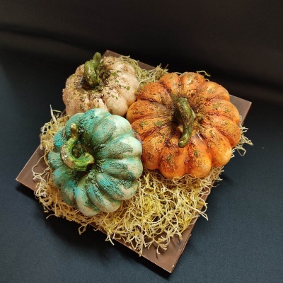 Três abóboras decorativas coloridas sobre palha num recipiente castanho