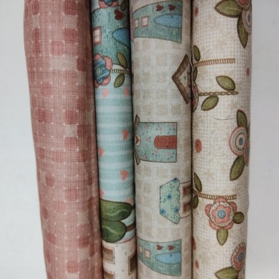 Rolos de tecido com padrões variados em rosa, azul, bege, casas e flores.