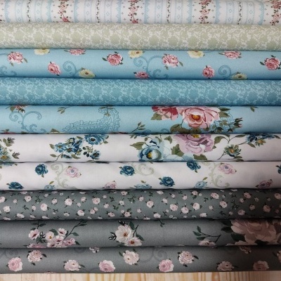 Tecidos florais em tons pastéis e azuis dispostos em rolos sobre madeira