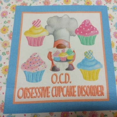 Tecido decorativo com padrão floral e painel central de cupcakes coloridos com texto