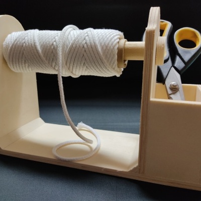 Suporte organizador de madeira com fio branco e tesoura preta e amarela sobre superfície escura