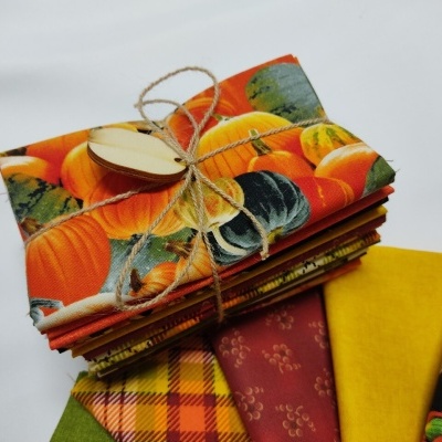 Conjunto de tecidos coloridos com padrões de abóboras e flores, amarrados com cordão e etiqueta de madeira