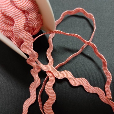 Fita rosa ondulada desenrolada de recipiente branco sobre superfície preta