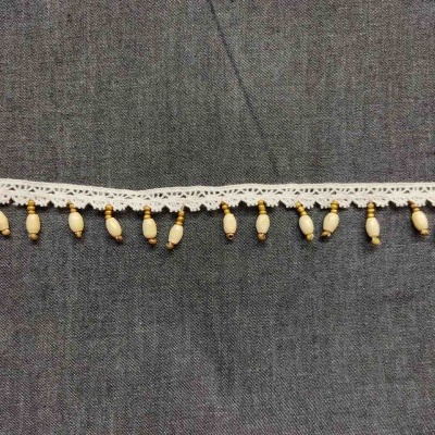 Fita decorativa branca com contas pendentes sobre tecido cinzento.