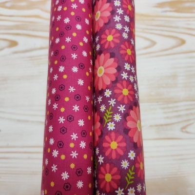 Dois rolos de tecido floral em fundo vermelho sobre madeira clara