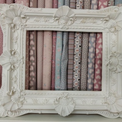 Moldura decorativa branca com ornamentos em relevo em frente a tecidos com diferentes padrões e cores pastel.