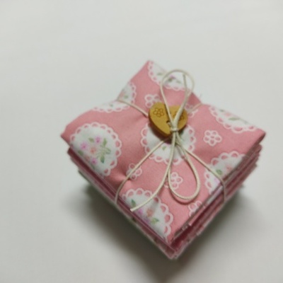 Conjunto de cinco panos de tecido rosa com padrões florais, amarrados com fio branco e botão de madeira