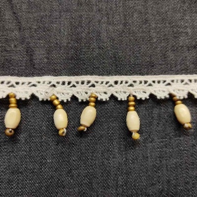 Franja de renda branca com contas de madeira e esferas amarelas penduradas sobre tecido escuro