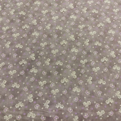Tecido castanho claro com padrão de pequenas flores brancas e lilases.