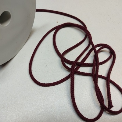 Cordão bordô trançado junto a carretel cinza claro sobre superfície branca