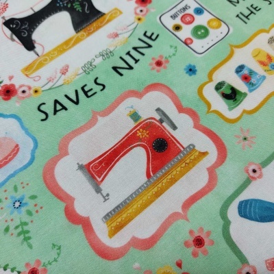 Tecido colorido com padrão de máquinas de costura, botões, flores e texto 'SAVES NINE'