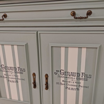 Móvel branco com riscas em bege e texto preto, puxadores metálicos bronze