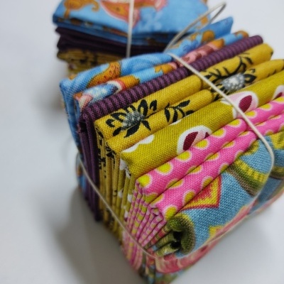 Conjunto de tecidos coloridos dobrados com padrões florais, abelhas e bolinhas, amarrados com fio.