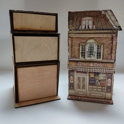 Conjunto de caixas de madeira empilhadas ao lado de caixa decorativa em forma de casinha com fachada de café chamada 'Gran Cafe'.