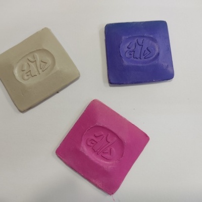 Três blocos quadrados de massa nas cores bege, azul e rosa com marca embutida.