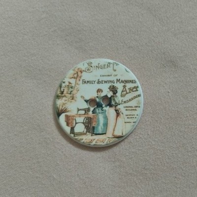 Botão decorativo redondo com ilustração vintage e texto relacionado com máquinas de costura Singer