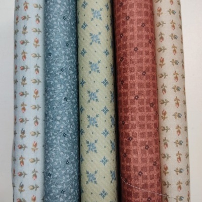 Cinco rolos de tecido com diferentes padrões pequenos e várias cores como branco, azul, amarelo e vermelho.