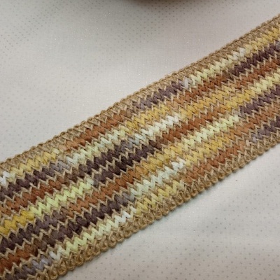 Ouvido de tecido com padrão em zig-zag nas cores castanho, bege, amarelo e branco sobre fundo branco.