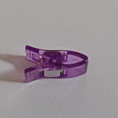 Prendedor pequeno de plástico roxo translúcido sobre superfície branca