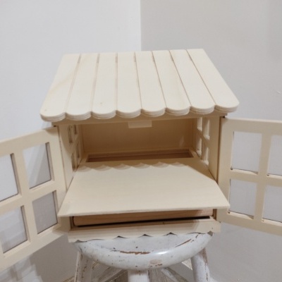 Casa de madeira branca com telhado de ripas e porta dupla aberta em cima de banco branco.