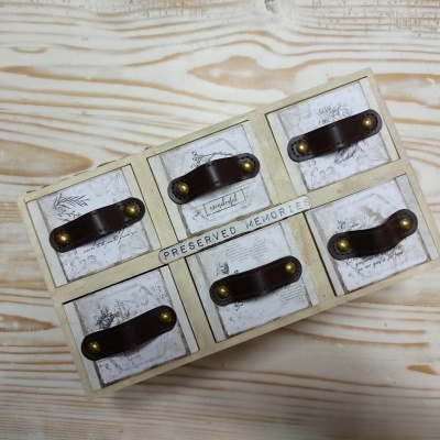 Caixa de madeira clara com seis gavetas pequenas e alças de couro castanho, frase 'PRESERVED MEMORIES'.