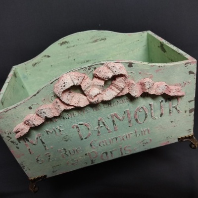 Caixa de madeira verde claro com ornamento rosa e texto envelhecido