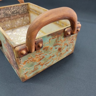 Cesto metálico envelhecido com pega de madeira sobre pano preto