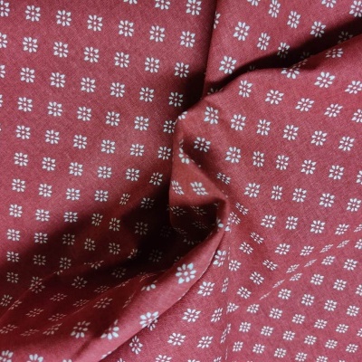 Tecido vermelho com padrão de pequenos quadrados brancos formando flores