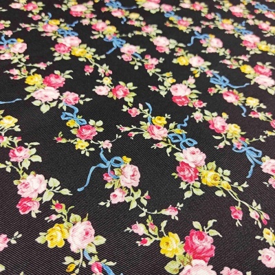 Tecido preto com padrão floral colorido, pequenas flores e laços azuis