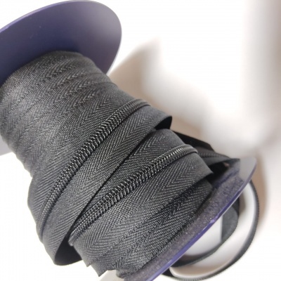 Fita têxtil preta com padrão espinha de peixe enrolada num carretel roxo.