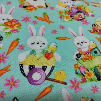 Tecido azul claro com padrão de coelhos, cenouras, flores, pintinhos e casas de pássaros