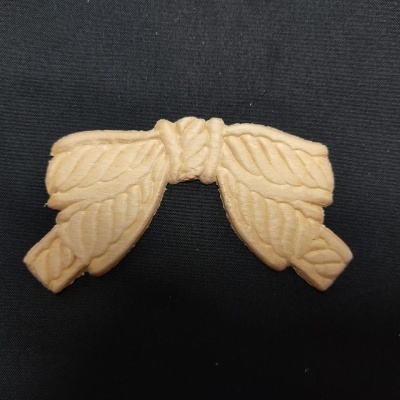 Peça decorativa de madeira clara em forma de laço sobre fundo preto