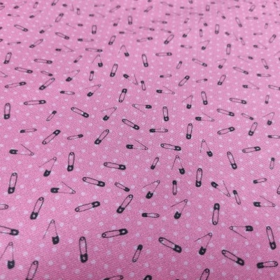 Tecido rosa com padrão de alfinetes de segurança pretos e brancos e pequenos pontos brancos no fundo