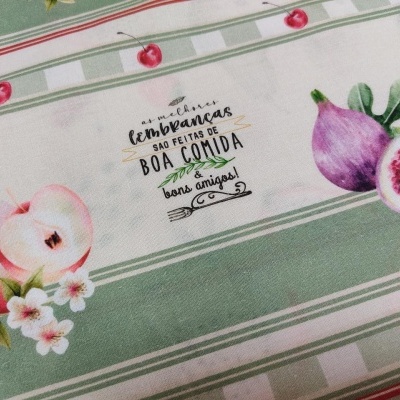 Pano de cozinha estampado com frutas, flores e texto em português.