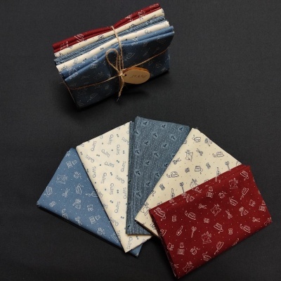 Cinco lenços de algodão em azul, creme e vermelho com padrões pequenos, amarrados com corda e etiqueta de madeira, sobre fundo preto