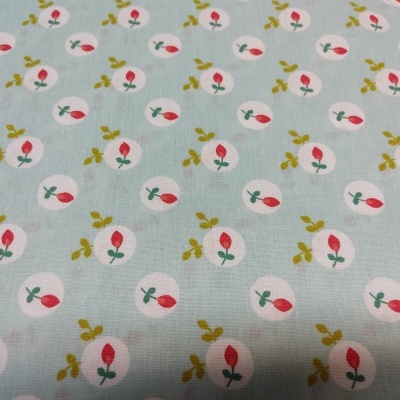 Tecido azul claro com padrão de pequenas flores cor-de-rosa e verdes em círculos brancos.