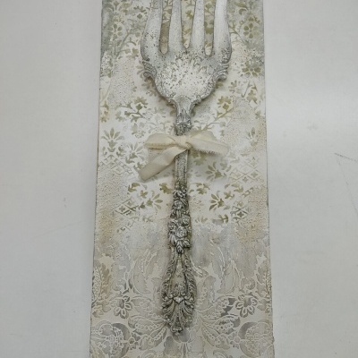 Garfo decorativo prateado com padrão floral numa placa decorativa bege